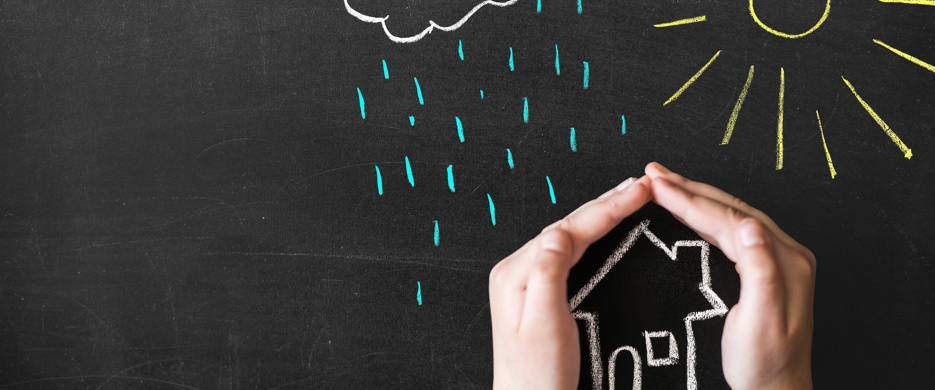 hands protecting house chalked on blackboard